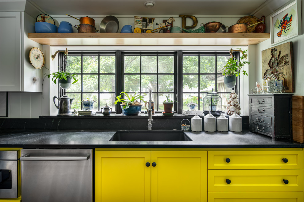 Photo of a mid-sized transitional l-shaped open plan kitchen in Kansas City with an undermount sink, shaker cabinets, yellow cabinets, soapstone benchtops, black splashback, timber splashback, coloured appliances, light hardwood floors, no island, brown floor, black benchtop and recessed.