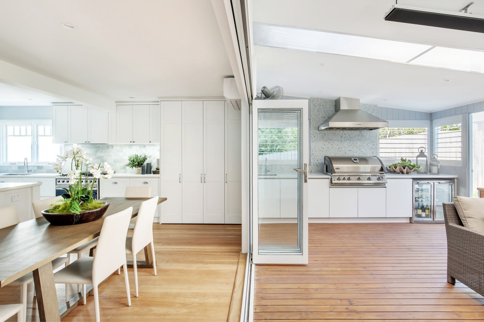 Modern inredning av ett stort vit linjärt vitt kök med öppen planlösning, med skåp i shakerstil, vita skåp, marmorbänkskiva, grönt stänkskydd, stänkskydd i tunnelbanekakel, rostfria vitvaror, mellanmörkt trägolv, en köksö och brunt golv
