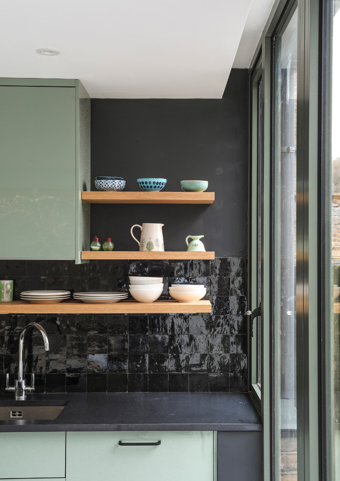Inspiration for a mid-sized contemporary single-wall open plan kitchen in London with a drop-in sink, flat-panel cabinets, green cabinets, solid surface benchtops, black splashback, ceramic splashback, stainless steel appliances, terrazzo floors, grey floor and black benchtop.