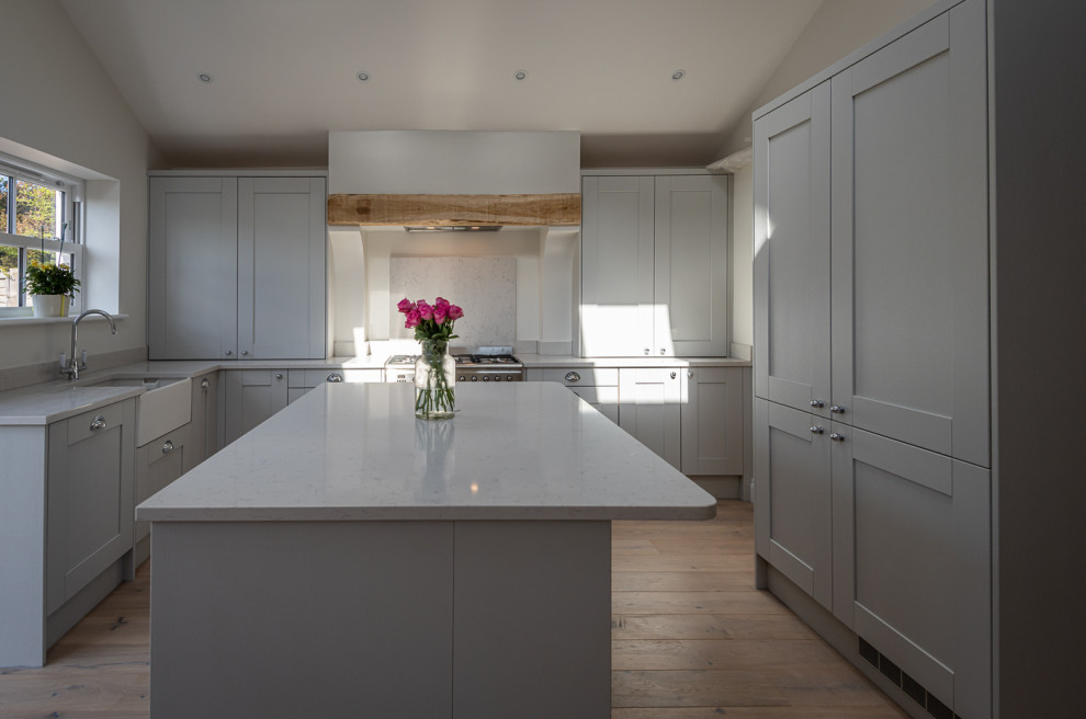 Beach style open plan kitchen in Kent with a farmhouse sink, shaker cabinets, grey cabinets, quartzite benchtops, white splashback, light hardwood floors, with island, white benchtop and vaulted.