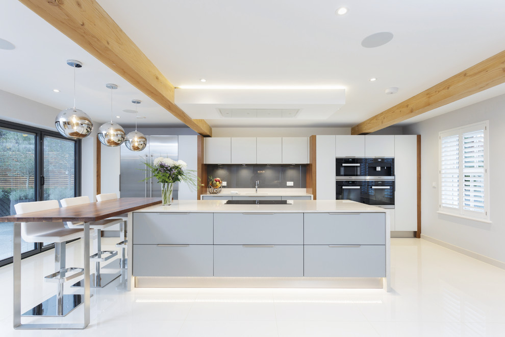 This is an example of a contemporary kitchen in Sussex with flat-panel cabinets, grey splashback, ceramic floors, white floor, white cabinets, glass sheet splashback, stainless steel appliances and multiple islands.