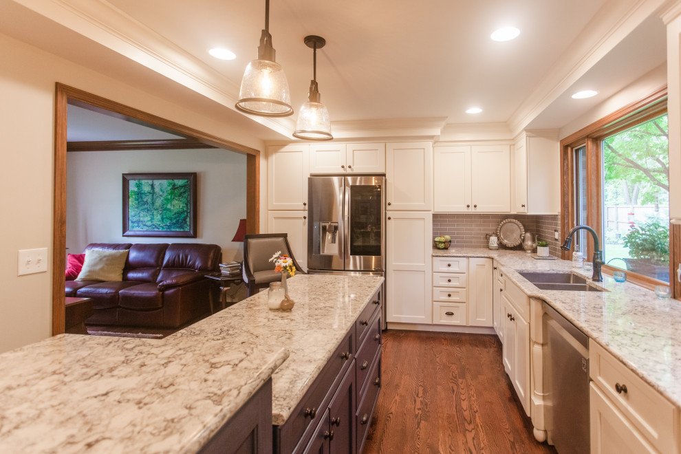 Eat-in kitchen - large transitional single-wall dark wood floor, brown floor and coffered ceiling eat-in kitchen idea in Cincinnati with a double-bowl sink, shaker cabinets, white cabinets, granite countertops, gray backsplash, subway tile backsplash, stainless steel appliances, an island and multicolored countertops