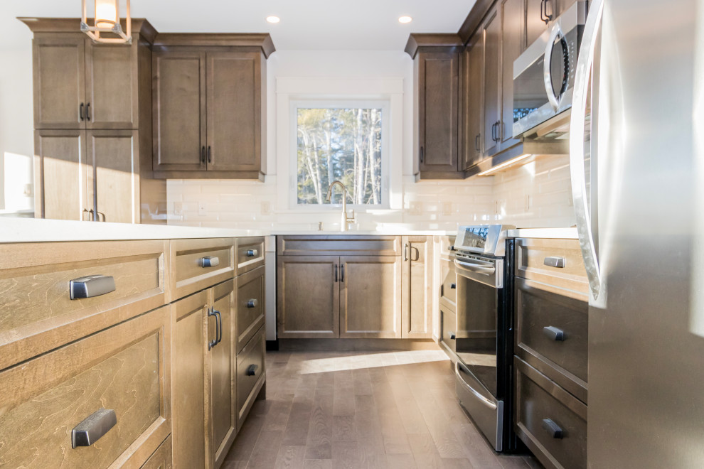 Example of a mid-sized l-shaped vinyl floor and brown floor kitchen design with a drop-in sink, recessed-panel cabinets, brown cabinets, quartzite countertops, white backsplash, subway tile backsplash, stainless steel appliances, an island and white countertops