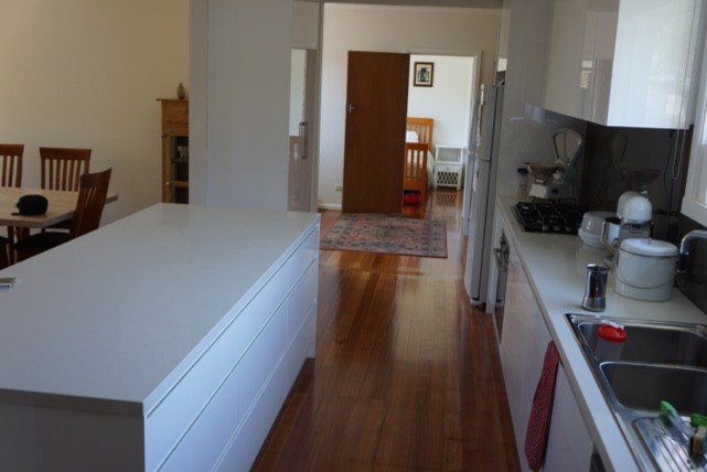 Photo of a large modern galley eat-in kitchen in Melbourne with flat-panel cabinets, white cabinets, quartz benchtops, black splashback, glass sheet splashback, a double-bowl sink, stainless steel appliances, medium hardwood floors, with island and white benchtop.
