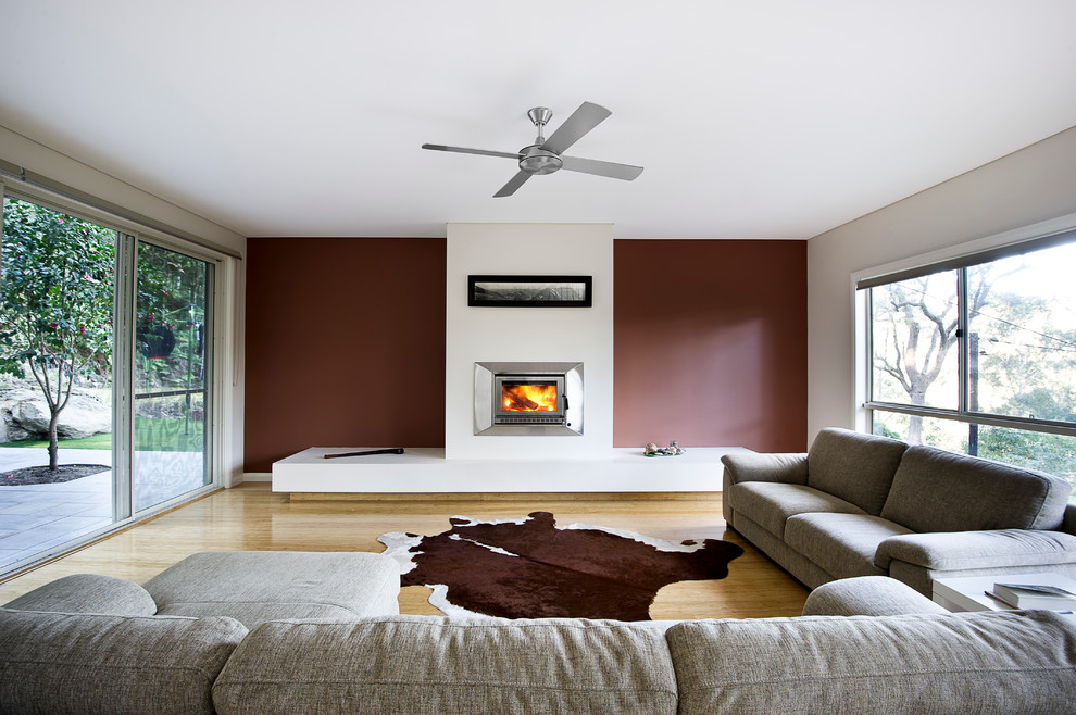 Design ideas for a large contemporary formal open concept living room in Sydney with red walls, bamboo floors, a standard fireplace, a plaster fireplace surround and no tv.