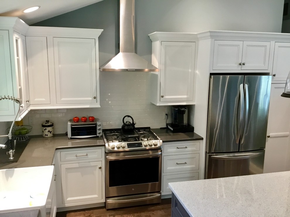 Mid-sized transitional l-shaped dark wood floor and brown floor kitchen photo in New York with a farmhouse sink, recessed-panel cabinets, white cabinets, granite countertops, white backsplash, subway tile backsplash, stainless steel appliances, an island and black countertops