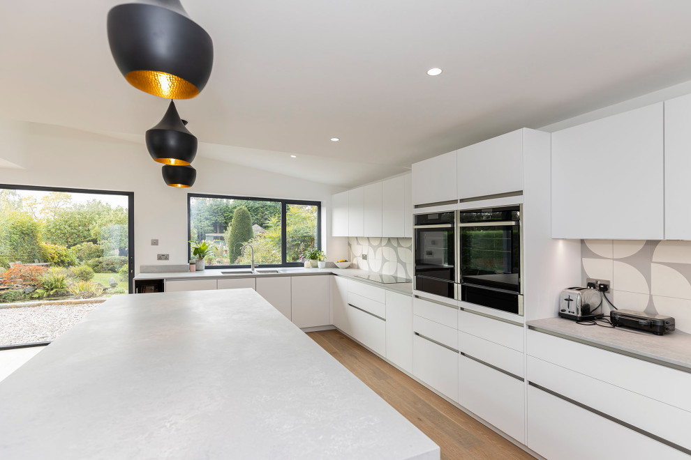 Inspiration for a large scandinavian open plan kitchen in Hertfordshire with a drop-in sink, recessed-panel cabinets, granite benchtops, mosaic tile splashback, black appliances, laminate floors, with island, beige floor and grey benchtop.