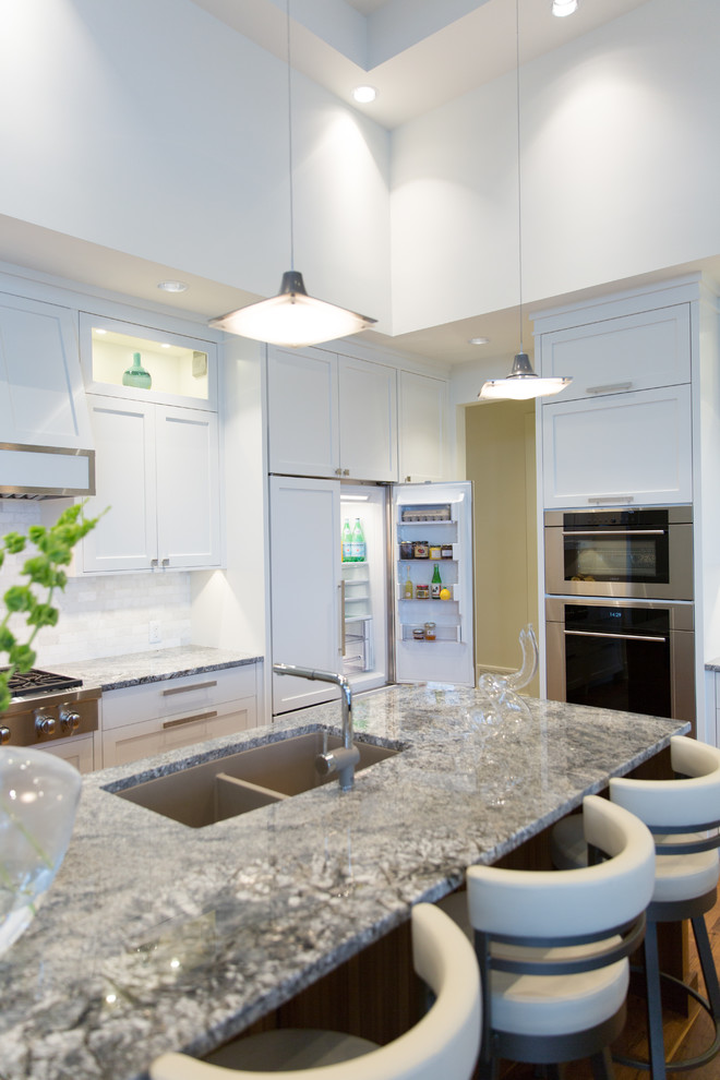 Example of a mid-sized transitional l-shaped medium tone wood floor eat-in kitchen design in Vancouver with shaker cabinets, white cabinets, granite countertops, white backsplash, white appliances, an island and an undermount sink