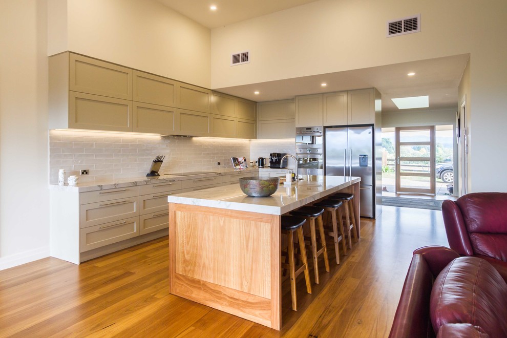 This is an example of an expansive contemporary l-shaped open plan kitchen in Melbourne with shaker cabinets, white splashback, subway tile splashback, stainless steel appliances, medium hardwood floors and with island.
