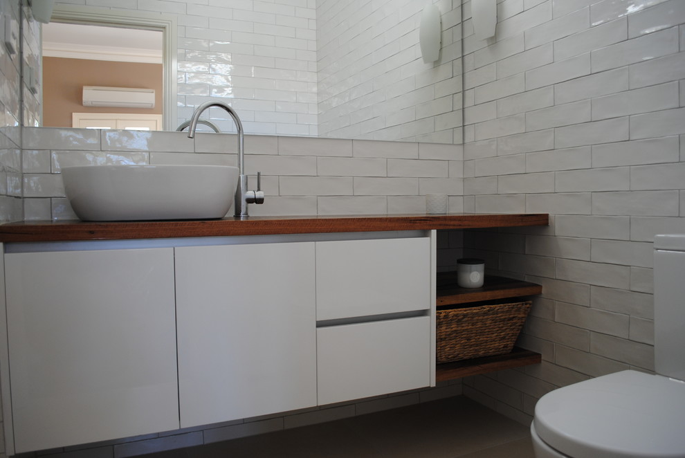 This is an example of a mid-sized contemporary master bathroom in Melbourne with white cabinets, an open shower, a one-piece toilet, white tile, ceramic tile, white walls, porcelain floors, a vessel sink, wood benchtops and furniture-like cabinets.