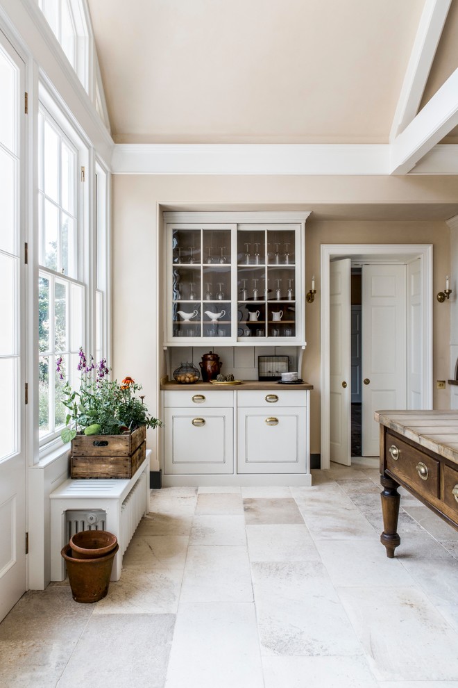 Photo of a large classic l-shaped kitchen in Hampshire with a belfast sink, distressed cabinets, marble worktops, white splashback, porcelain splashback, black appliances, limestone flooring, an island, beige floors and white worktops.