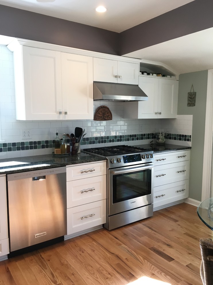Inspiration for a mid-sized transitional l-shaped light wood floor enclosed kitchen remodel with an undermount sink, flat-panel cabinets, white cabinets, granite countertops, white backsplash, subway tile backsplash, stainless steel appliances and no island