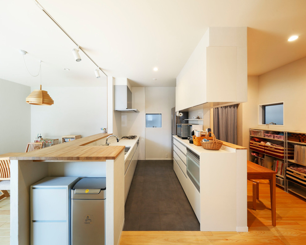 Scandinavian single-wall open plan kitchen in Osaka with a single-bowl sink, flat-panel cabinets, white cabinets, white splashback, a peninsula and black floor.