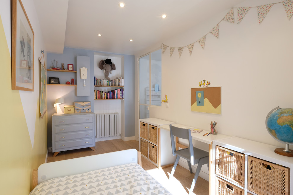 This is an example of a mid-sized scandinavian gender-neutral kids' bedroom for kids 4-10 years old in Paris with blue walls and light hardwood floors.