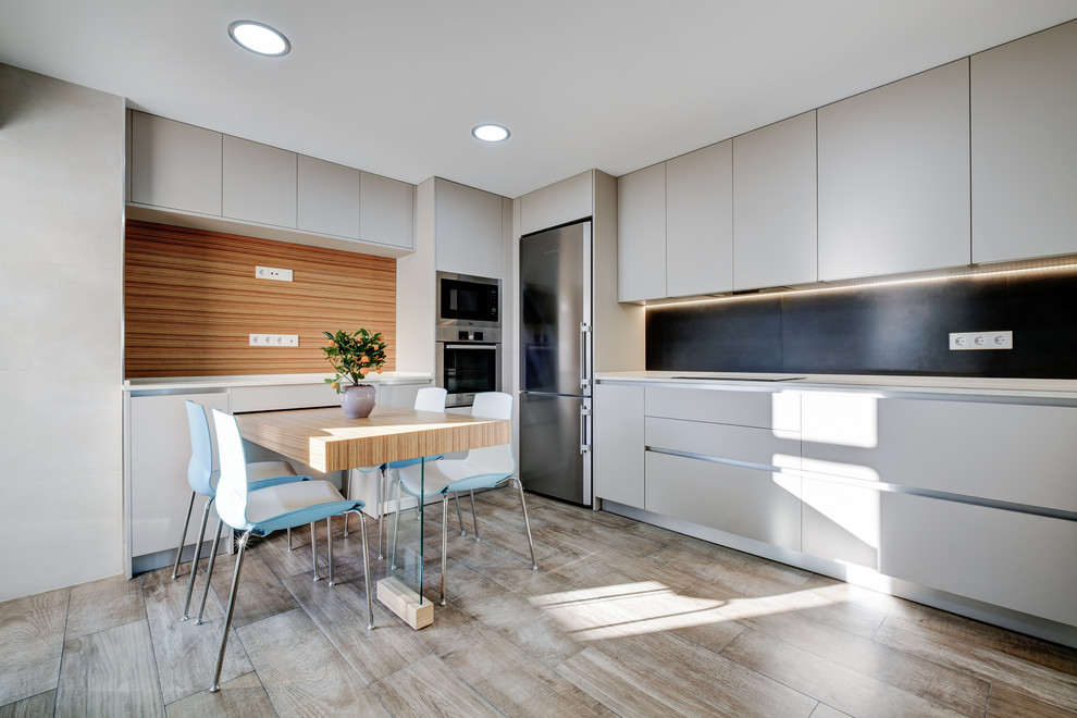 Design ideas for a modern l-shaped eat-in kitchen in Madrid with flat-panel cabinets, black splashback, stainless steel appliances and no island.