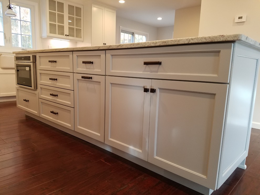 Inspiration for a mid-sized transitional l-shaped dark wood floor and brown floor eat-in kitchen remodel with a farmhouse sink, shaker cabinets, white cabinets, granite countertops, white backsplash, subway tile backsplash, stainless steel appliances and an island