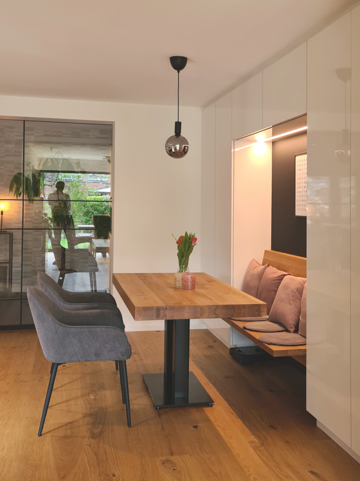 Inspiration for a medium sized contemporary kitchen in Dusseldorf with flat-panel cabinets, white cabinets, black splashback, black appliances, medium hardwood flooring, an island and black worktops.