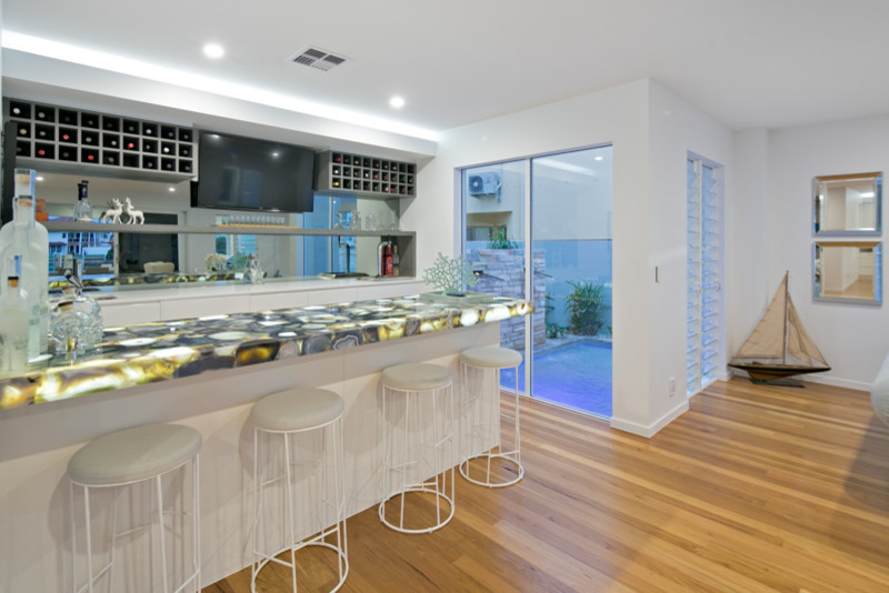 Inspiration for an expansive beach style galley seated home bar in Brisbane with an undermount sink, quartz benchtops, multi-coloured splashback, mirror splashback, light hardwood floors and beige floor.