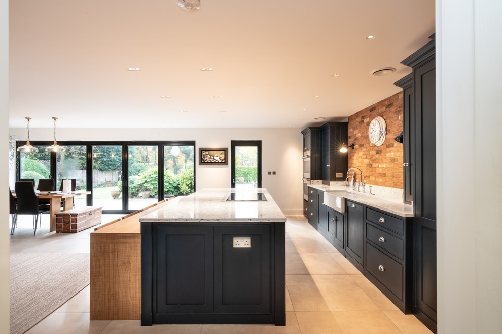 Expansive contemporary single-wall open plan kitchen in Essex with a farmhouse sink, beaded inset cabinets, blue cabinets, quartzite benchtops, multi-coloured splashback, brick splashback, stainless steel appliances, terra-cotta floors, with island, beige floor and white benchtop.