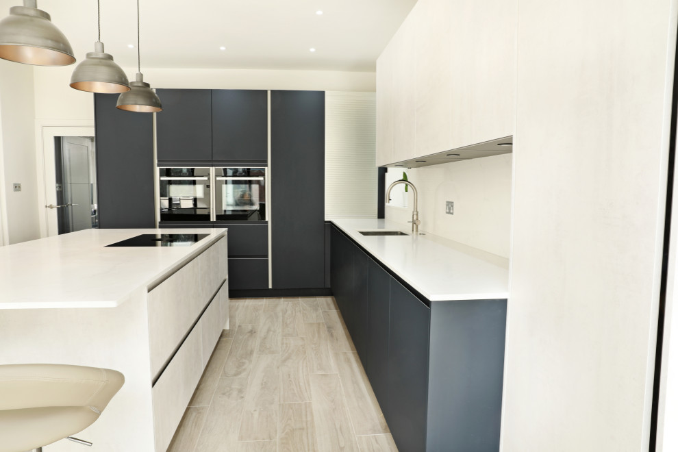 This is an example of a large contemporary l-shaped kitchen/diner in London with a built-in sink, flat-panel cabinets, blue cabinets, quartz worktops, white splashback, stone slab splashback, black appliances, laminate floors, an island, grey floors, white worktops and feature lighting.