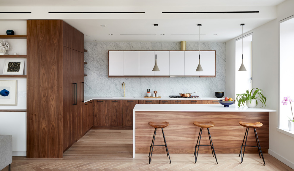 Design ideas for a mid-sized midcentury l-shaped separate kitchen in New York with an undermount sink, flat-panel cabinets, dark wood cabinets, solid surface benchtops, grey splashback, stone slab splashback, panelled appliances, light hardwood floors, a peninsula, beige floor and white benchtop.