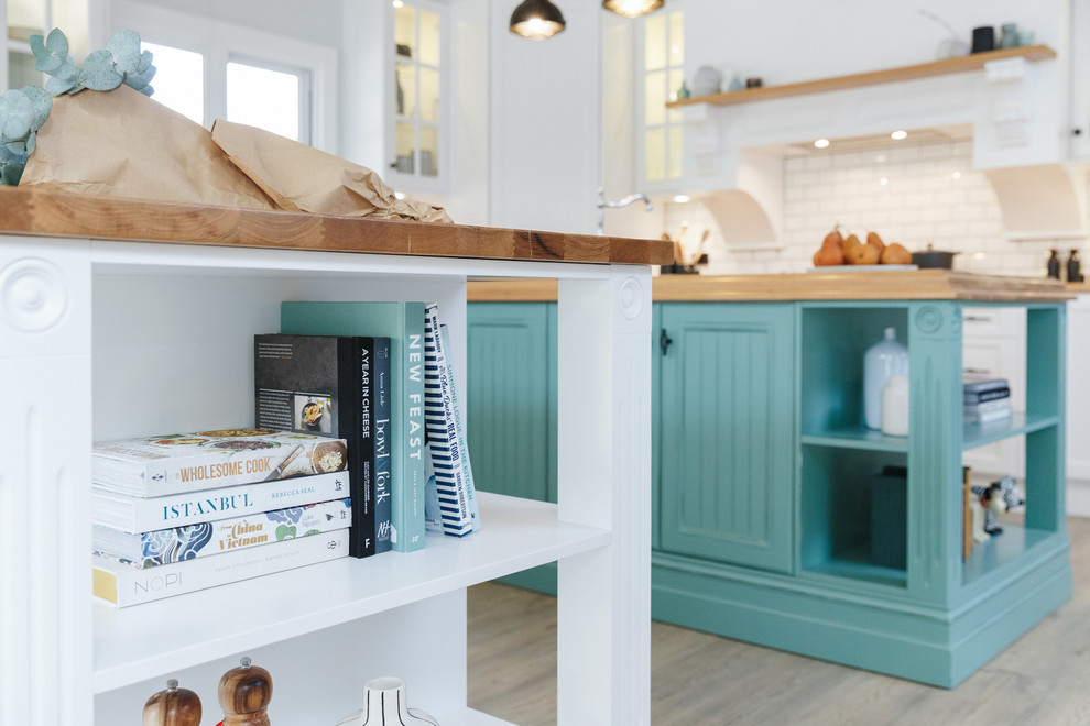 This is an example of a large transitional u-shaped open plan kitchen in Adelaide with a farmhouse sink, shaker cabinets, white cabinets, wood benchtops, white splashback, subway tile splashback, stainless steel appliances, medium hardwood floors and multiple islands.