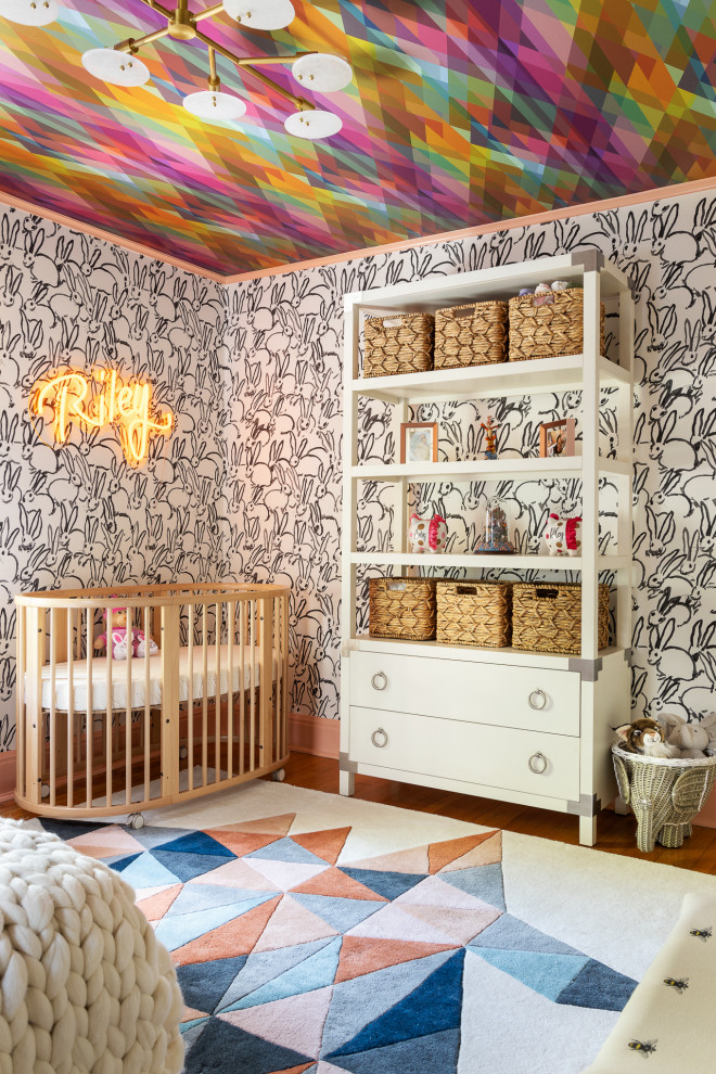 Diseño de habitación de bebé neutra ecléctica de tamaño medio con paredes blancas, suelo de madera clara, suelo marrón, papel pintado y papel pintado