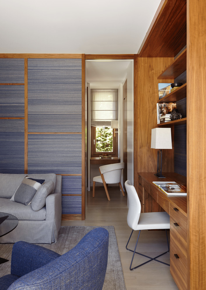 This is an example of a beach style home office in New York with blue walls, light hardwood floors and a built-in desk.