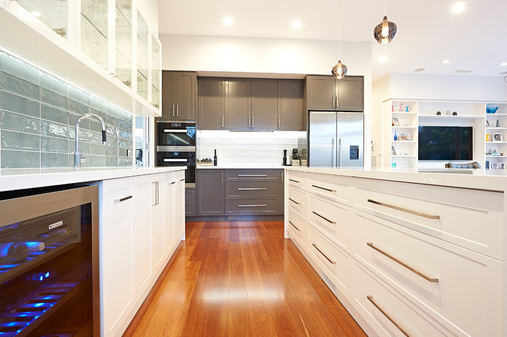 Large contemporary l-shaped open plan kitchen in Melbourne with a double-bowl sink, beaded inset cabinets, white cabinets, quartz benchtops, white splashback, porcelain splashback, stainless steel appliances, medium hardwood floors and with island.