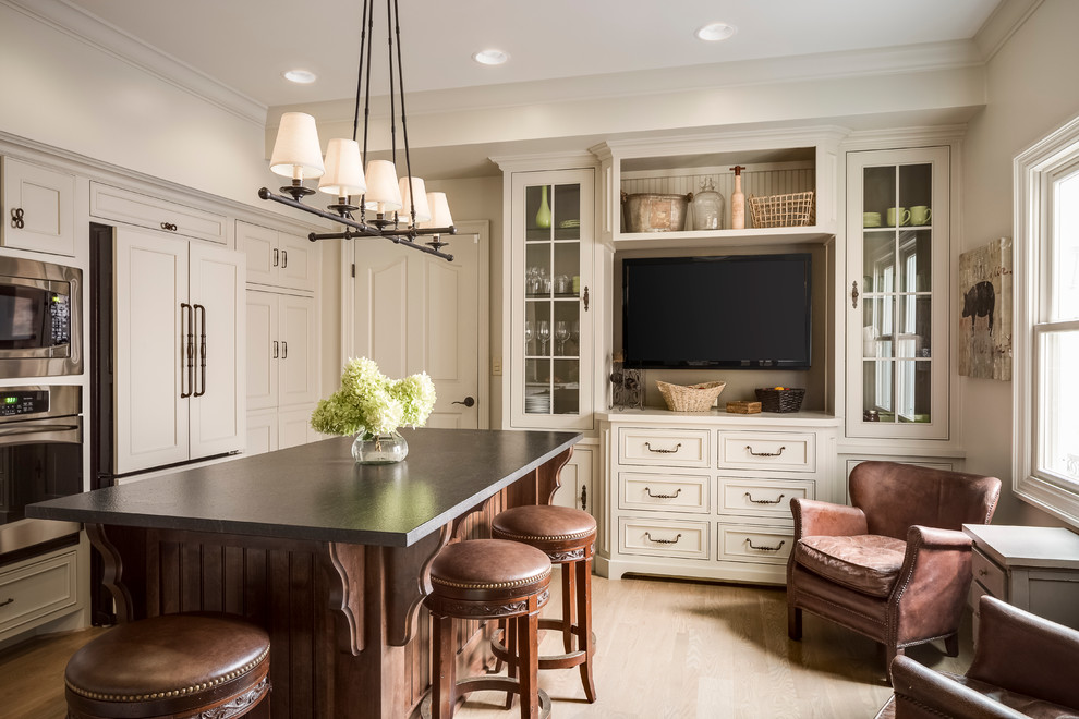 Inspiration for a traditional kitchen in Kansas City with a farmhouse sink, beaded inset cabinets, beige cabinets, granite benchtops, glass tile splashback, panelled appliances, light hardwood floors and with island.