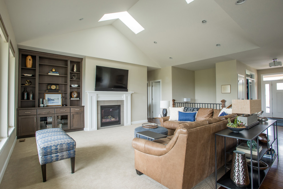 This is an example of a large transitional open concept family room in Denver with beige walls, carpet, a standard fireplace, a tile fireplace surround, a wall-mounted tv and beige floor.