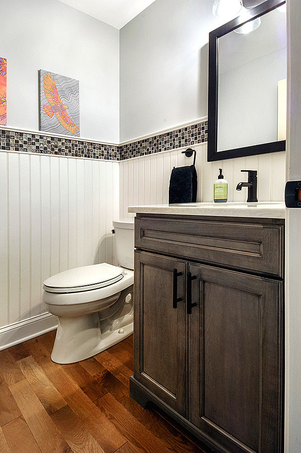 Design ideas for a transitional powder room in Philadelphia with recessed-panel cabinets, grey cabinets, a two-piece toilet, blue tile, mosaic tile, blue walls, medium hardwood floors, an undermount sink, engineered quartz benchtops, brown floor and white benchtops.