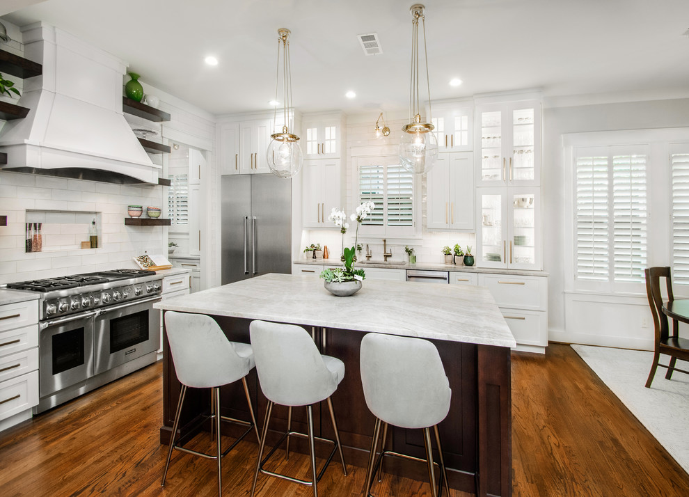 This is an example of a large transitional l-shaped open plan kitchen in Dallas with a drop-in sink, flat-panel cabinets, white cabinets, quartzite benchtops, white splashback, ceramic splashback, stainless steel appliances, dark hardwood floors, with island, brown floor and grey benchtop.