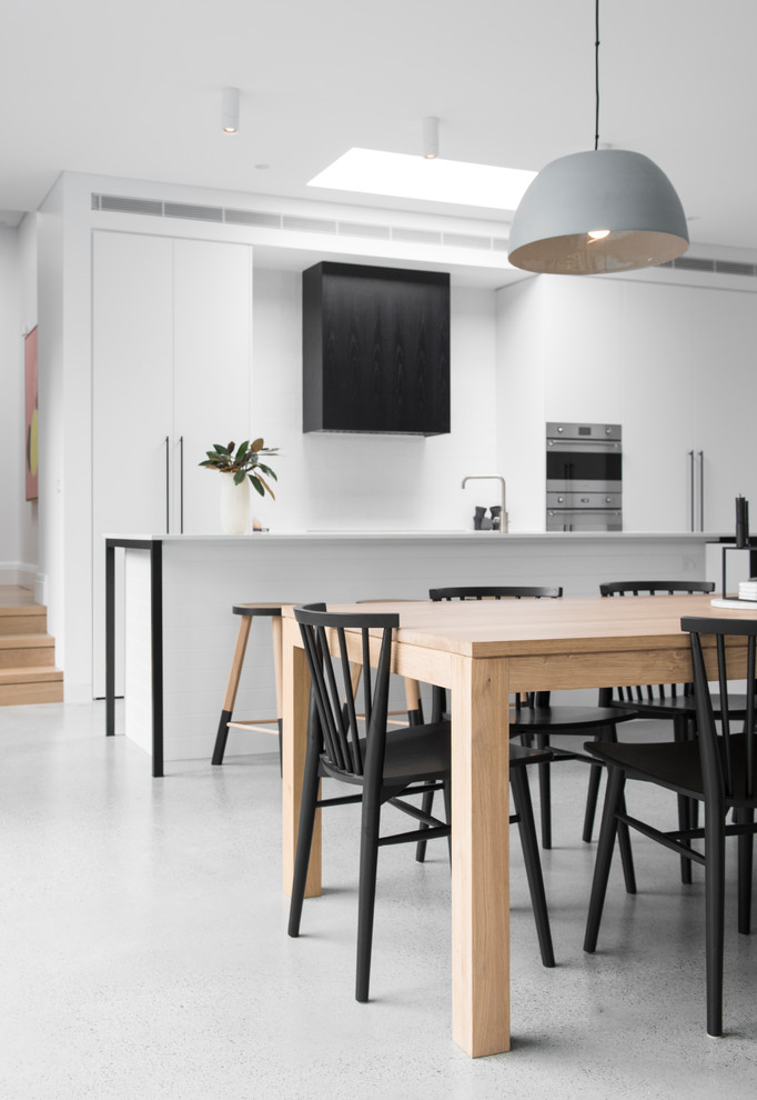 Design ideas for a large modern galley eat-in kitchen in Sydney with an undermount sink, flat-panel cabinets, white cabinets, solid surface benchtops, white splashback, ceramic splashback, panelled appliances, concrete floors, with island and grey floor.