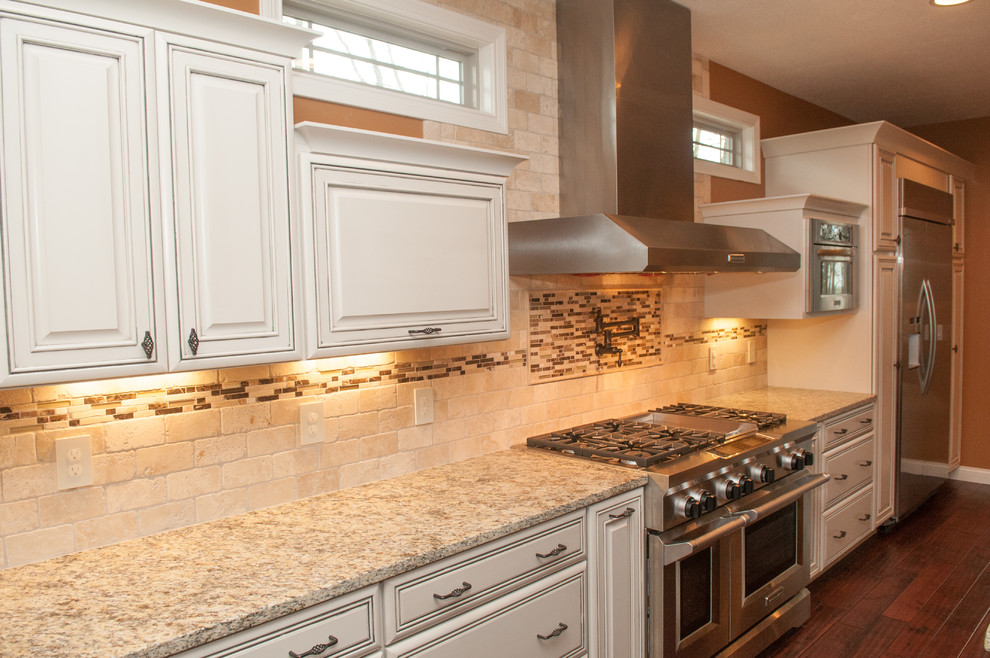 Example of a large trendy l-shaped dark wood floor and brown floor open concept kitchen design with beaded inset cabinets, white cabinets, granite countertops, beige backsplash, stone tile backsplash, stainless steel appliances, an island and a farmhouse sink