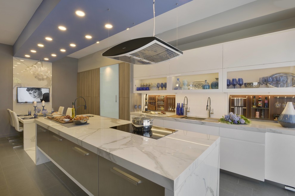 Photo of an expansive contemporary galley eat-in kitchen in New York with an undermount sink, flat-panel cabinets, tile benchtops, white splashback, timber splashback, panelled appliances, porcelain floors, with island, grey floor, white benchtop and stainless steel cabinets.
