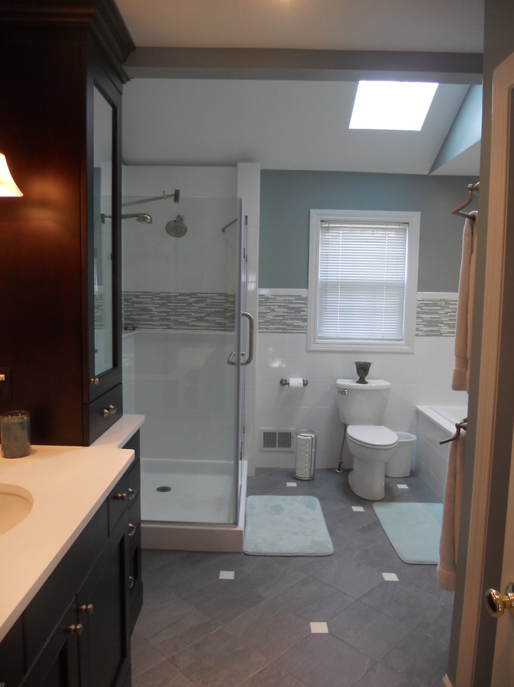 Example of a large transitional master gray tile and stone tile ceramic tile corner bathtub design with an undermount sink, recessed-panel cabinets, dark wood cabinets, quartz countertops, a two-piece toilet and gray walls