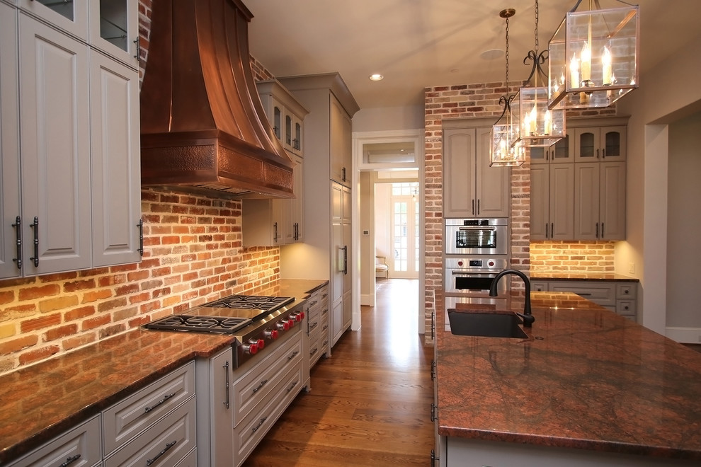 This is an example of a mid-sized traditional l-shaped eat-in kitchen in Houston with raised-panel cabinets, with island, an undermount sink, beige cabinets, red splashback, stone tile splashback, stainless steel appliances and medium hardwood floors.