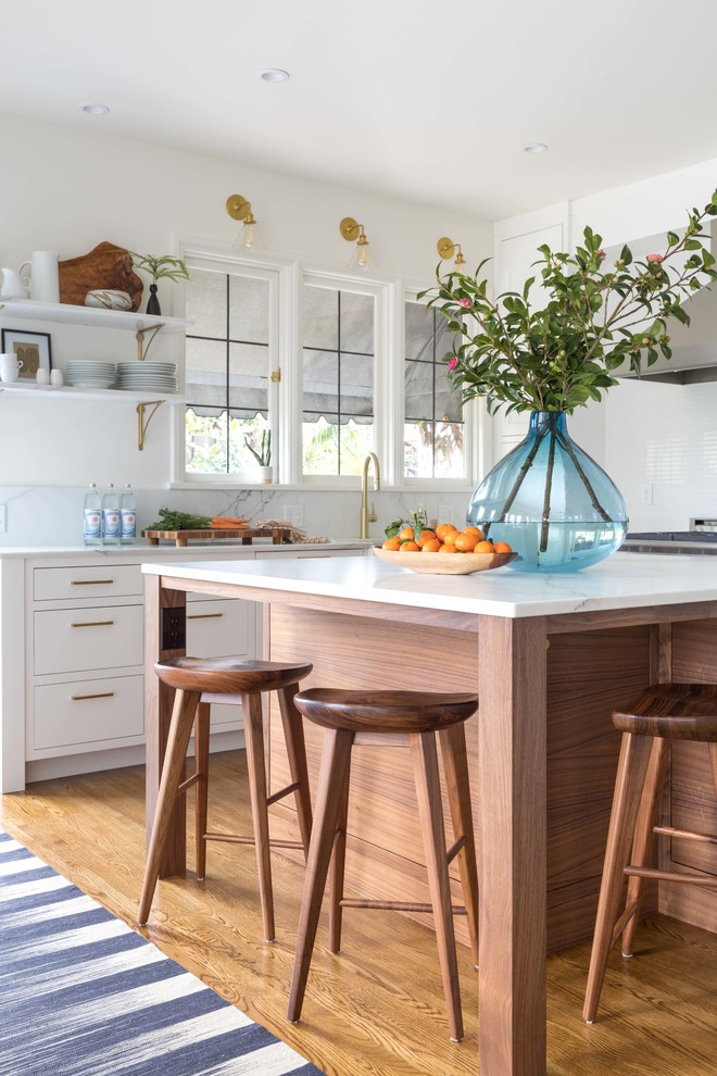Photo of a transitional l-shaped kitchen in Portland with flat-panel cabinets, white cabinets, white splashback, medium hardwood floors, with island and brown floor.