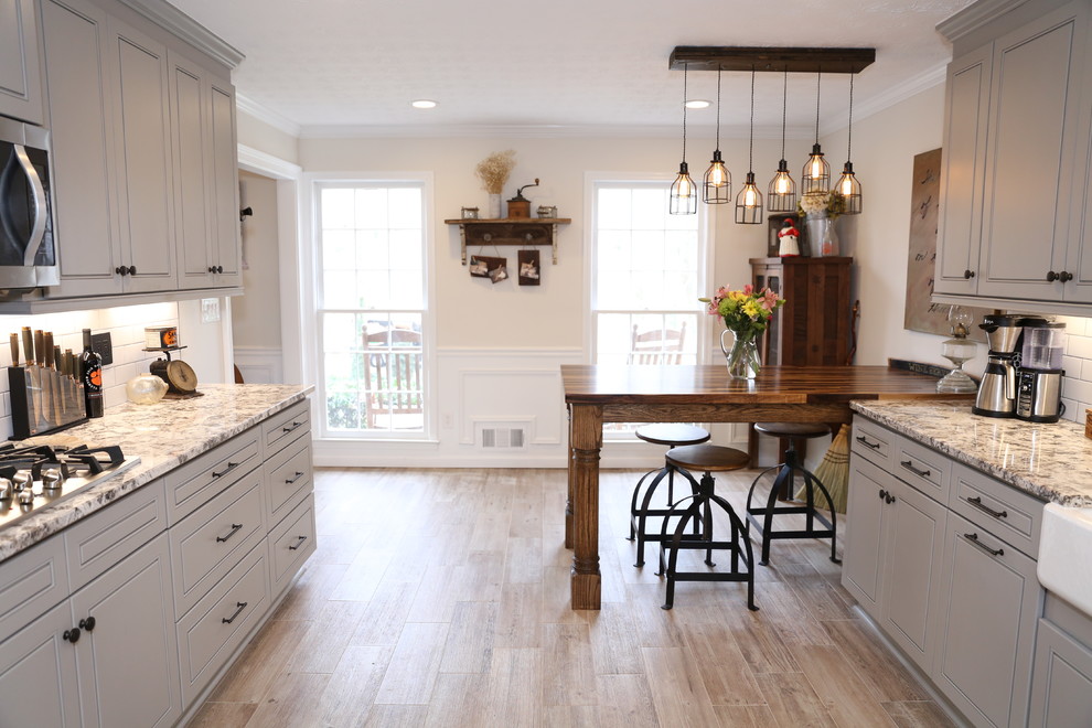 Large country galley eat-in kitchen in Atlanta with a farmhouse sink, raised-panel cabinets, grey cabinets, white splashback, stainless steel appliances, light hardwood floors, a peninsula and brown floor.