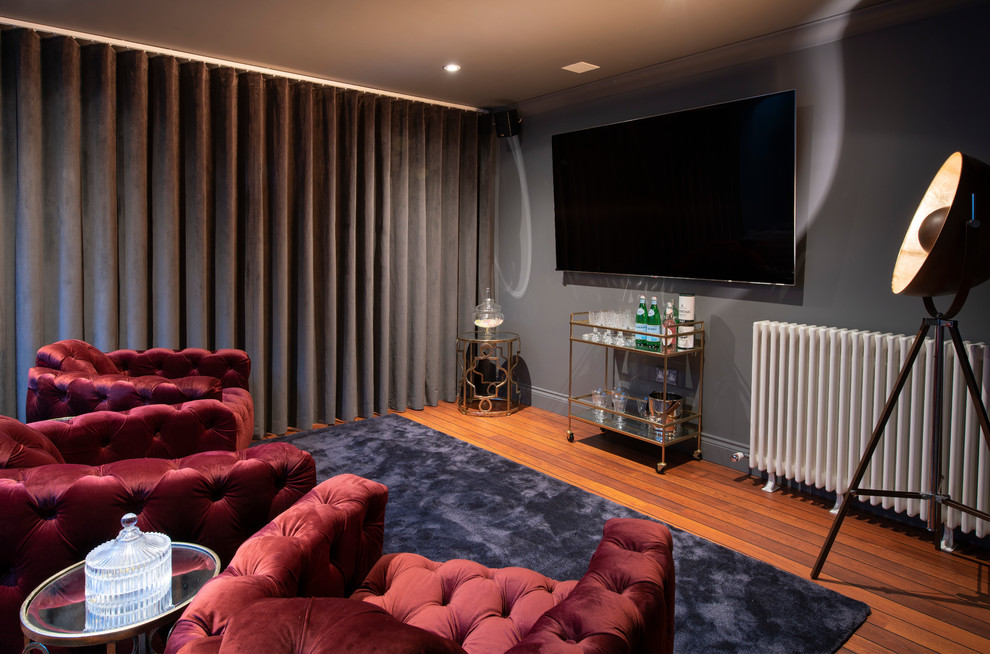 Inspiration for a large transitional open concept home theatre in Kent with grey walls, medium hardwood floors, a wall-mounted tv and brown floor.