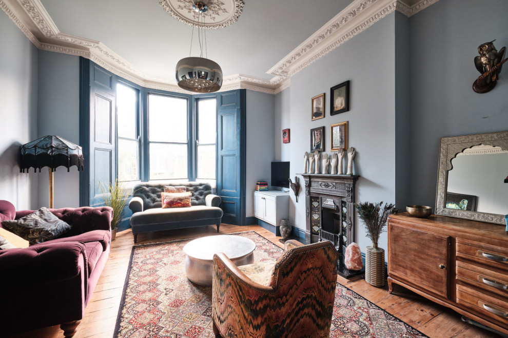 This is an example of a large bohemian open plan living room in London with blue walls, medium hardwood flooring, a standard fireplace, a metal fireplace surround, a wall mounted tv and a chimney breast.