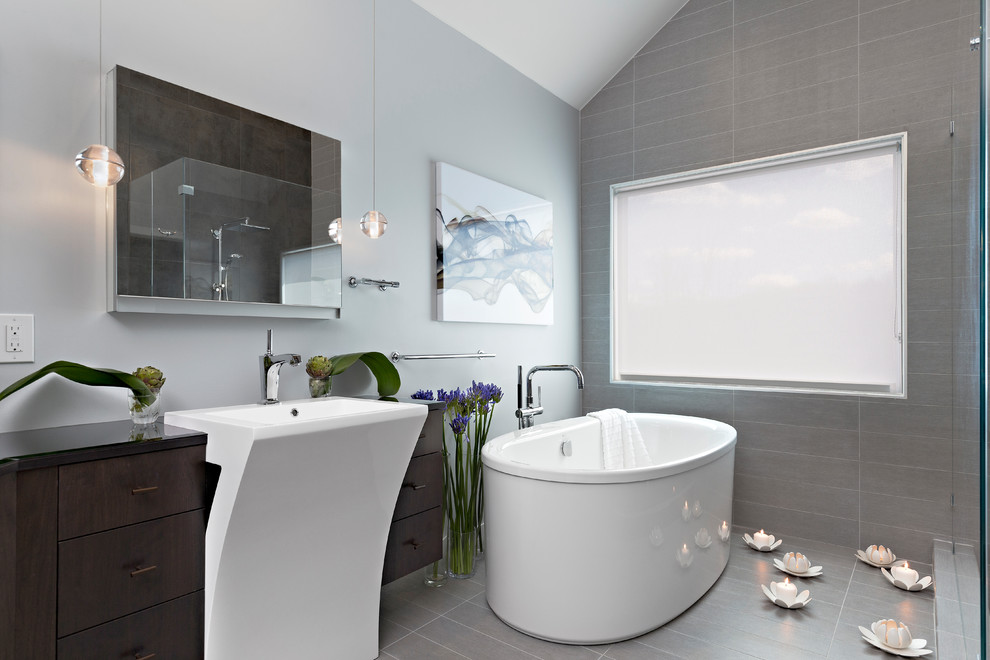 Contemporary master bathroom in Other with flat-panel cabinets, dark wood cabinets, a freestanding tub, grey walls, porcelain floors, a pedestal sink, gray tile, porcelain tile and grey floor.