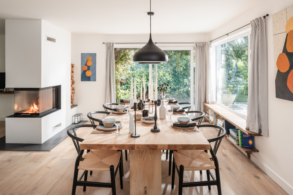 Inspiration for a large scandinavian dining room in Cornwall with white walls, light hardwood floors, a two-sided fireplace and a plaster fireplace surround.