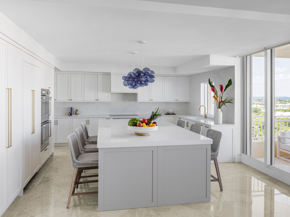 Immagine di un grande cucina con isola centrale stile marinaro con ante a filo, ante bianche, paraspruzzi bianco, elettrodomestici da incasso e top bianco