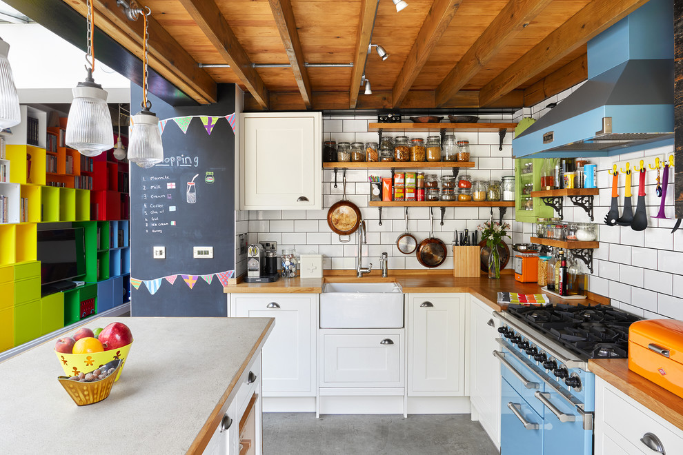 Photo of a mid-sized eclectic l-shaped open plan kitchen in London with a farmhouse sink, shaker cabinets, white cabinets, wood benchtops, white splashback, ceramic splashback, coloured appliances, concrete floors and with island.