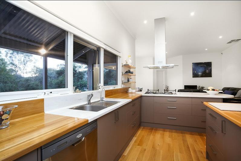 Inspiration for a mid-sized contemporary l-shaped eat-in kitchen in Melbourne with a double-bowl sink, flat-panel cabinets, brown cabinets, solid surface benchtops, stainless steel appliances and light hardwood floors.