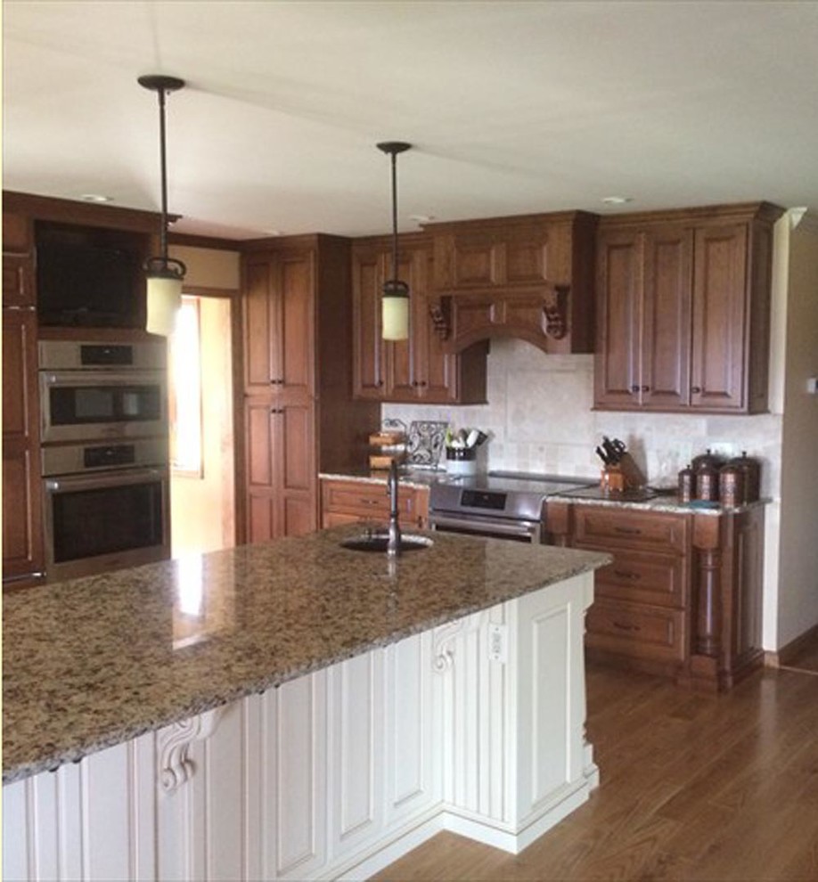 This is an example of a traditional l-shaped kitchen in Other with raised-panel cabinets, distressed cabinets, granite benchtops, stainless steel appliances, light hardwood floors and a peninsula.