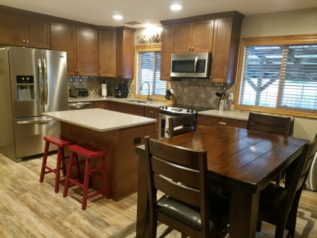 Small transitional l-shaped laminate floor and beige floor eat-in kitchen photo in Omaha with an undermount sink, shaker cabinets, medium tone wood cabinets, quartz countertops, gray backsplash, stone tile backsplash, stainless steel appliances, an island and gray countertops