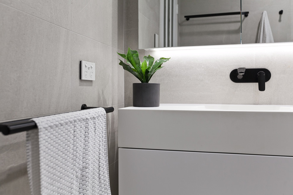 This is an example of a small contemporary 3/4 bathroom in Perth with flat-panel cabinets, white cabinets, a two-piece toilet, beige tile, porcelain tile, beige walls, porcelain floors, an integrated sink, solid surface benchtops, beige floor, a sliding shower screen and white benchtops.